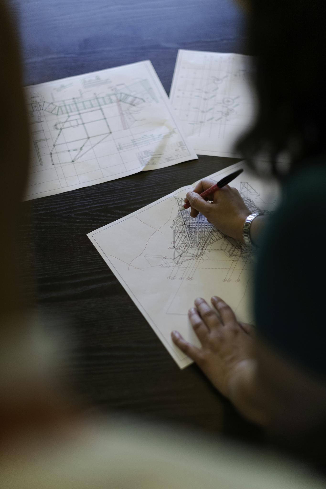 Female engineer working on detailed architectural blueprints on a wooden desk.