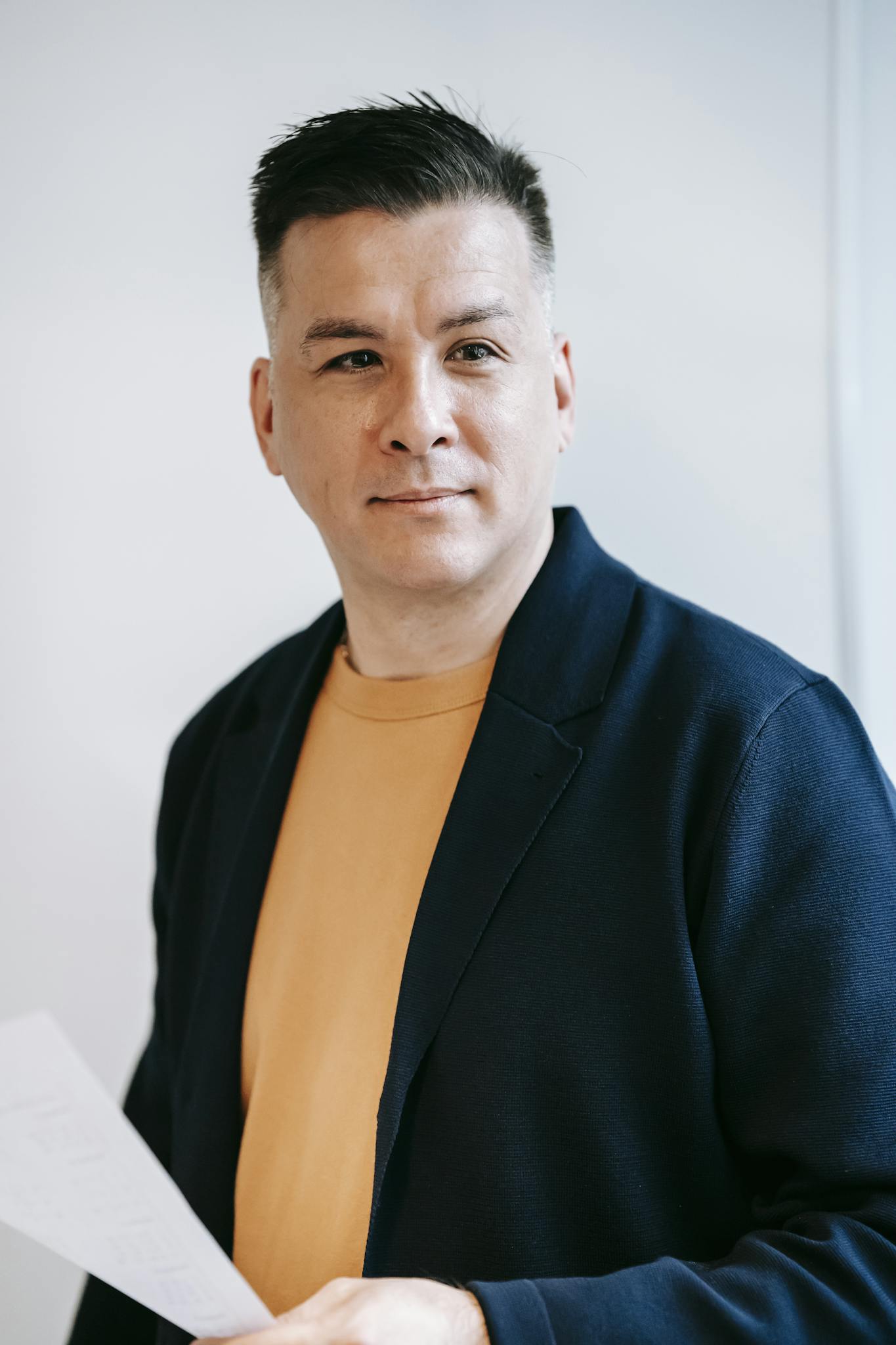 Portrait of a confident adult man in a blazer, holding paper, showcasing professional and stylish attire.